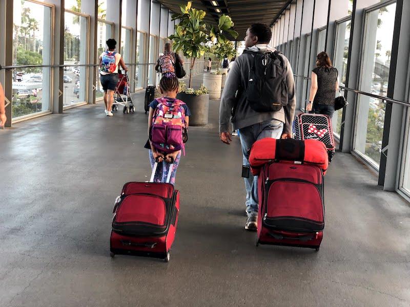 Black family strolling through an airport with luggage. Family travel, family vacation. Trusted traveler program